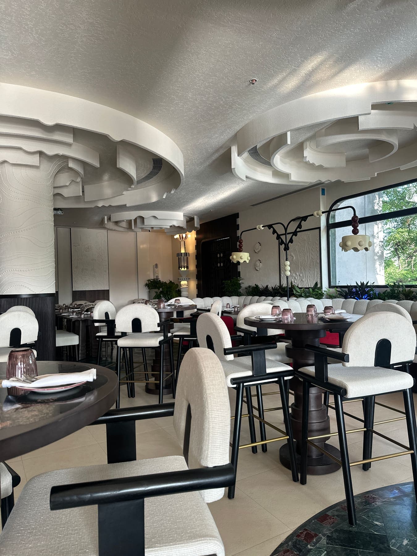 Restaurant dining room beneath a layered, sculpted plaster ceiling with cream boucle chairs and dark timber tables