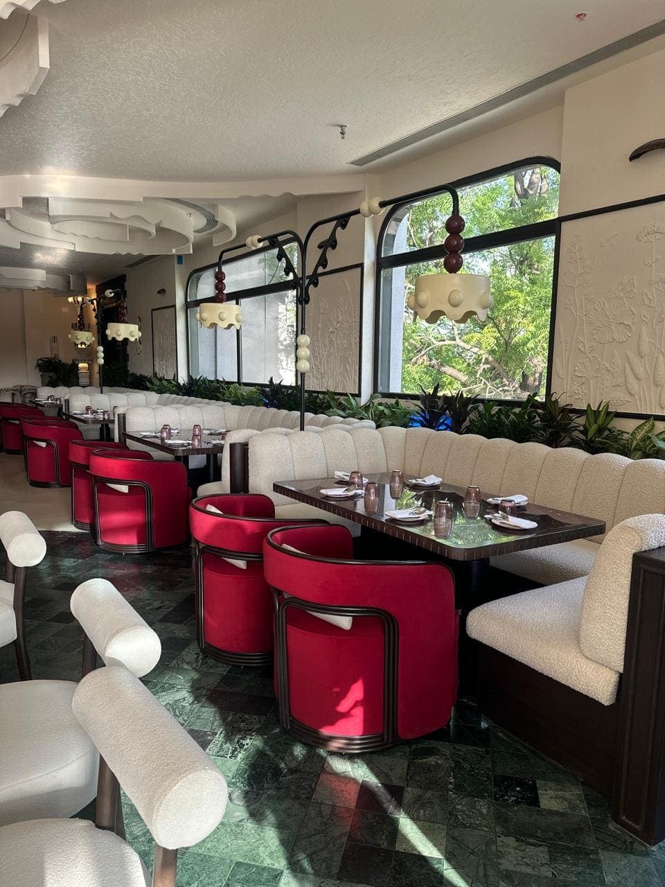 Red velvet chairs and a cream banquette along the windows, green marble floor
