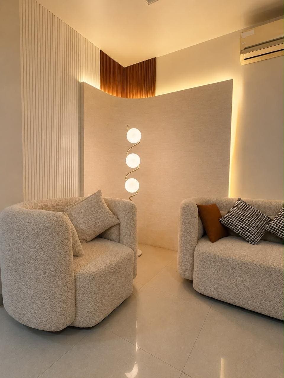 Boucle armchair and sofa beside a curved plaster wall lit by a concealed cove, with an orb floor lamp